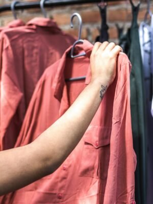 A close-up shot of a hand holding a salmon-colored shirt on a clothing rack.