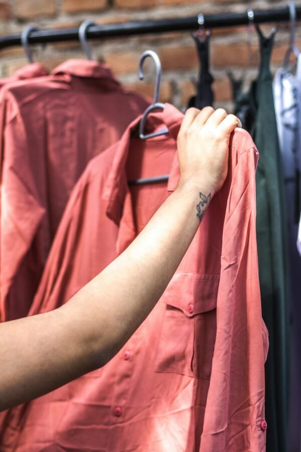 A close-up shot of a hand holding a salmon-colored shirt on a clothing rack.