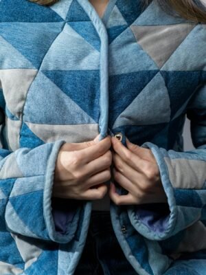 Close-up of a woman buttoning a geometric-patterned denim jacket, showcasing detailed fabric texture.