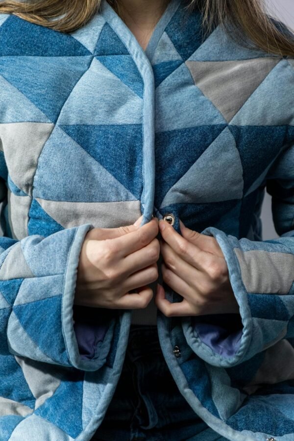 Close-up of a woman buttoning a geometric-patterned denim jacket, showcasing detailed fabric texture.