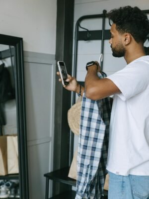 Young man holding a plaid shirt and using smartphone for online shopping. Casual indoor setting.